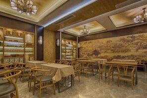 A dining area with tables and chairs, a wall with a mural, and shelves with items on the left. - West Lake Teavilla (Hangzhou)