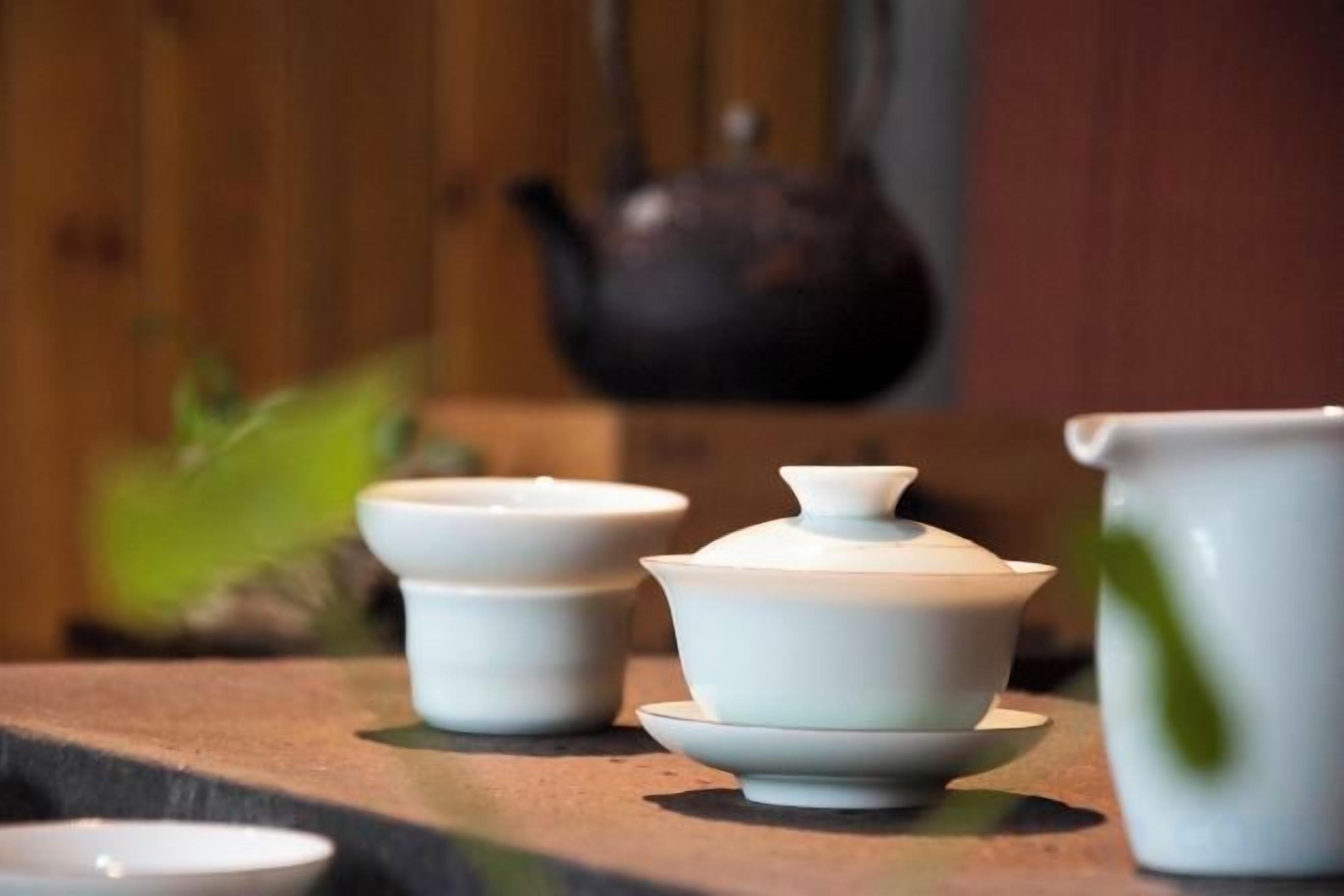 Un juego de tazas de té blancas de cerámica y una tetera sobre una superficie de madera.