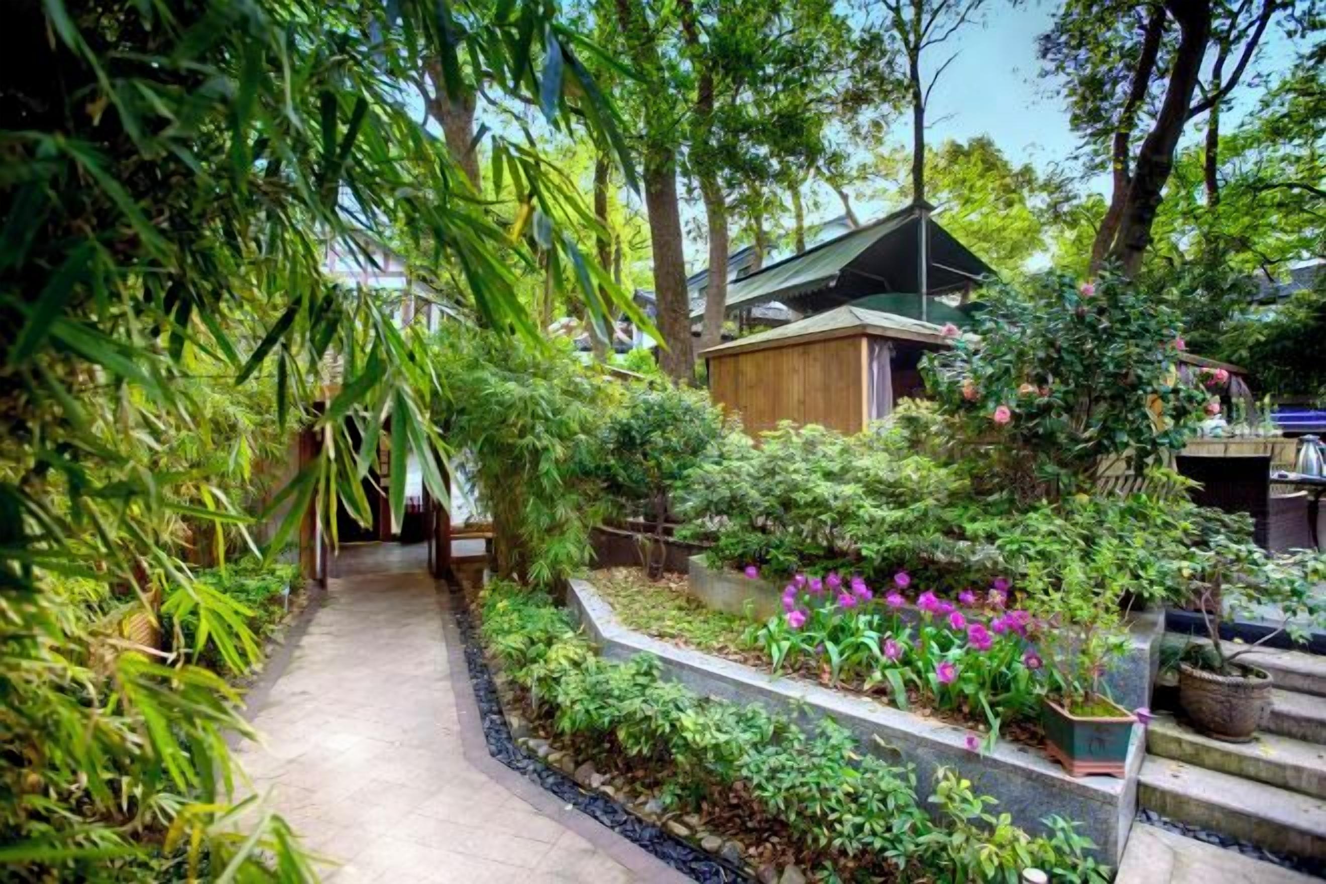 A pathway leading to a building surrounded by lush greenery and flowering plants.