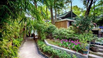 A pathway leading to a building surrounded by lush greenery and flowering plants.