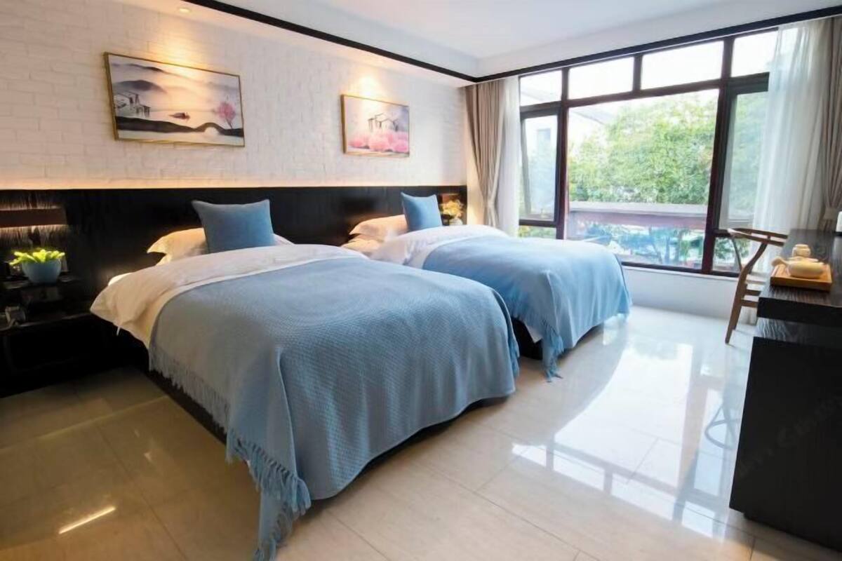 A hotel room with two beds, a large window, and artwork on the walls.