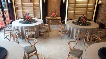 Un comedor de hotel con mesas y sillas redondas, una estantería y flores decorativas.