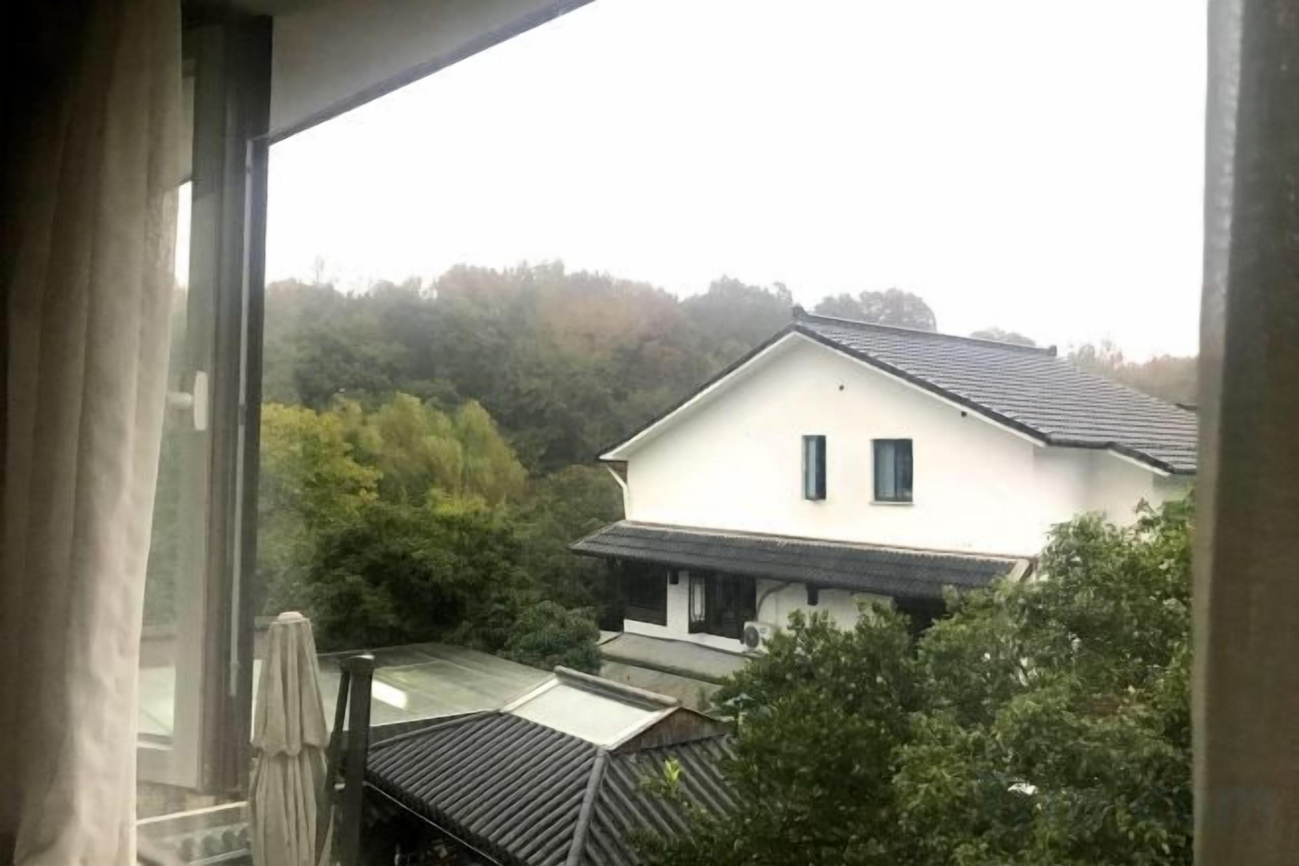 Vista de una casa con techo inclinado y fachada blanca, rodeada de árboles.