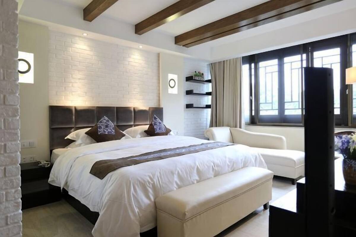 A modern bedroom with a large bed, a sofa, a TV, and a brick wall.