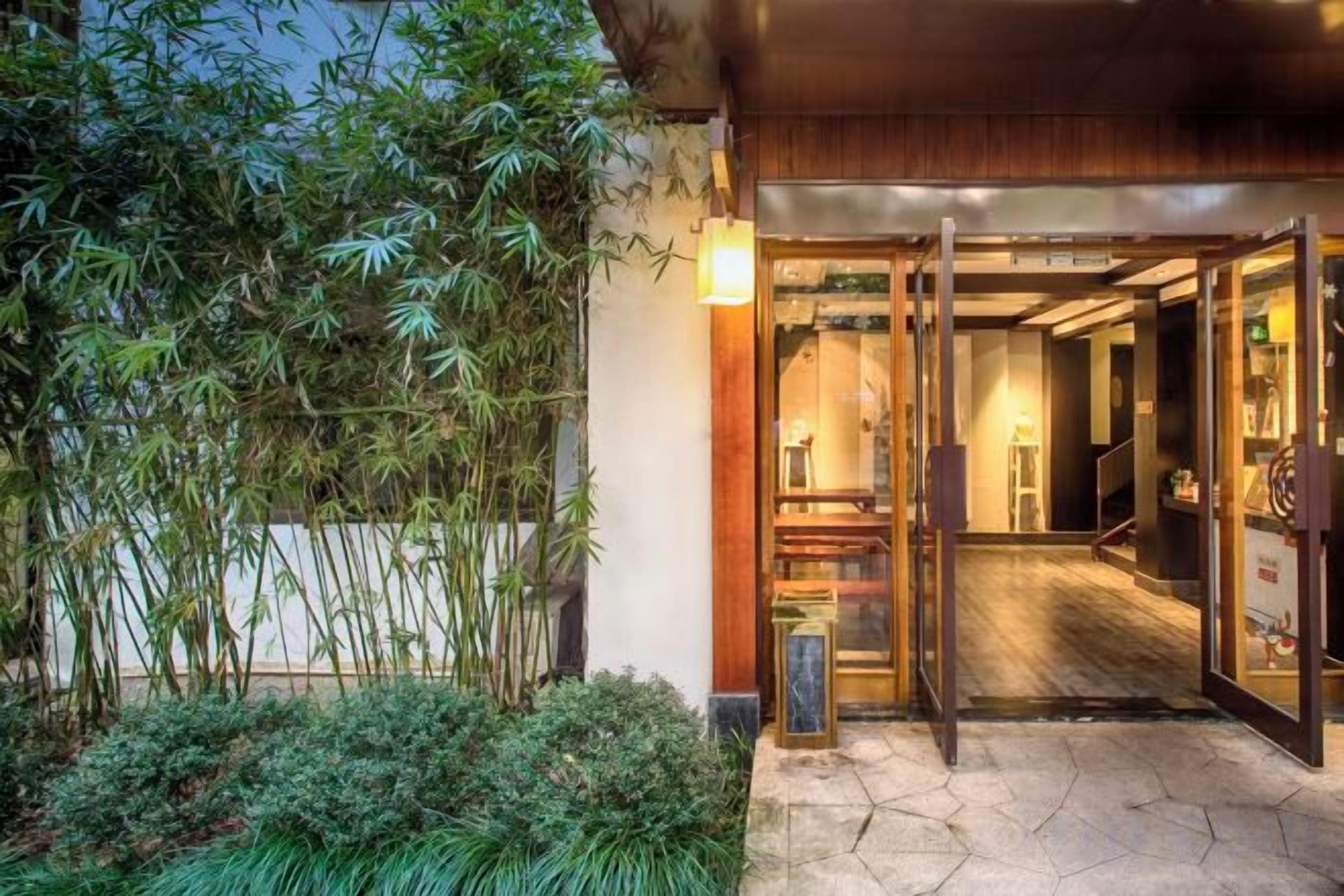 An entrance with a wooden door, a small garden with bamboo, and a tiled floor.