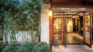 Una entrada con puerta de madera, un pequeño jardín de bambú y un suelo de baldosas.