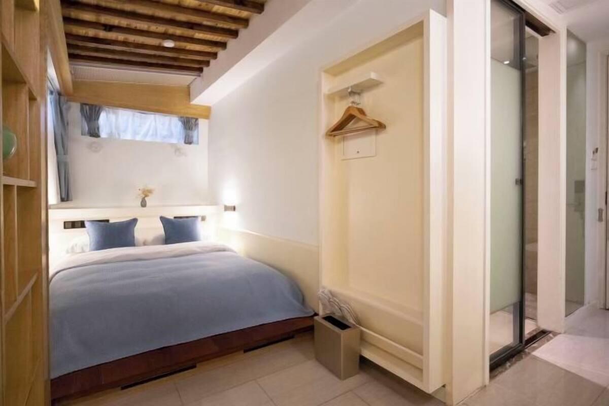 A bedroom with a bed, a hanging light, a mirror, and a door leading to another room.