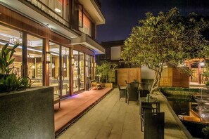 Un patio al aire libre con asientos, una pequeña fuente de agua y un edificio bien iluminado con puertas de cristal.