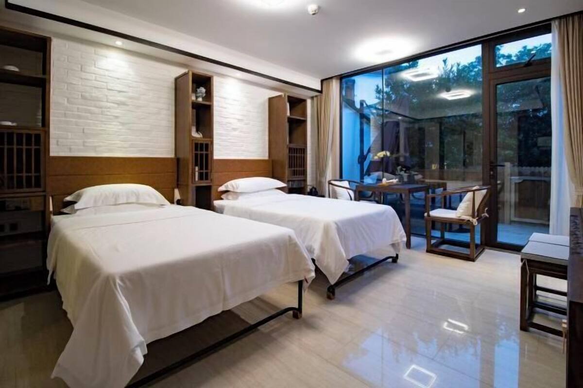 A hotel room with two beds, a desk, and a large window.
