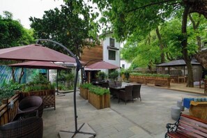 An outdoor patio with wicker furniture, a dining table, and umbrellas. - West Lake Teavilla (Hangzhou)