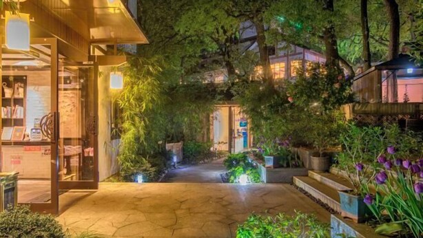 A well-lit outdoor area with a pathway leading to a building entrance, surrounded by lush greenery and potted plants. - West Lake Teavilla (Hangzhou)