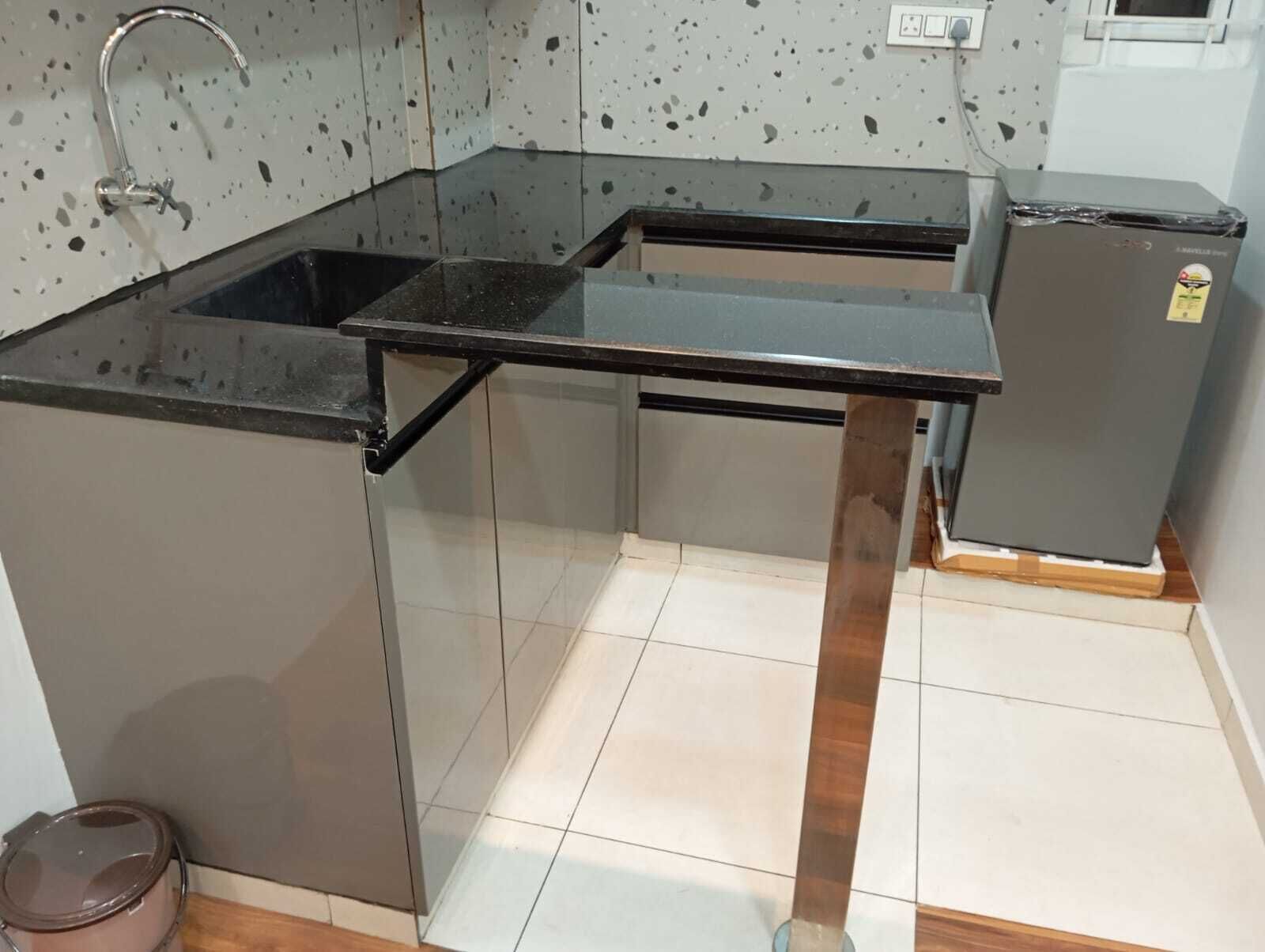 Una cocina con encimera negra, pileta de acero inoxidable y un refrigerador pequeño.