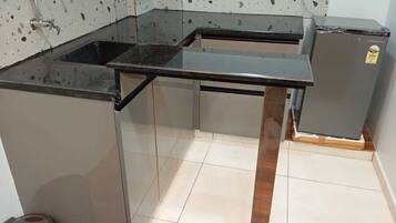 Una cocina con encimera negra, pileta de acero inoxidable y un refrigerador pequeño.