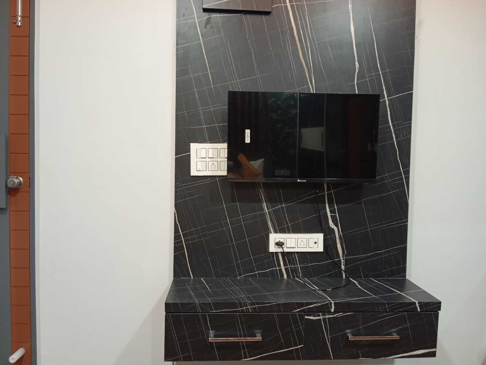 A black marble wall with a flat-screen TV mounted above a black marble cabinet with drawers.