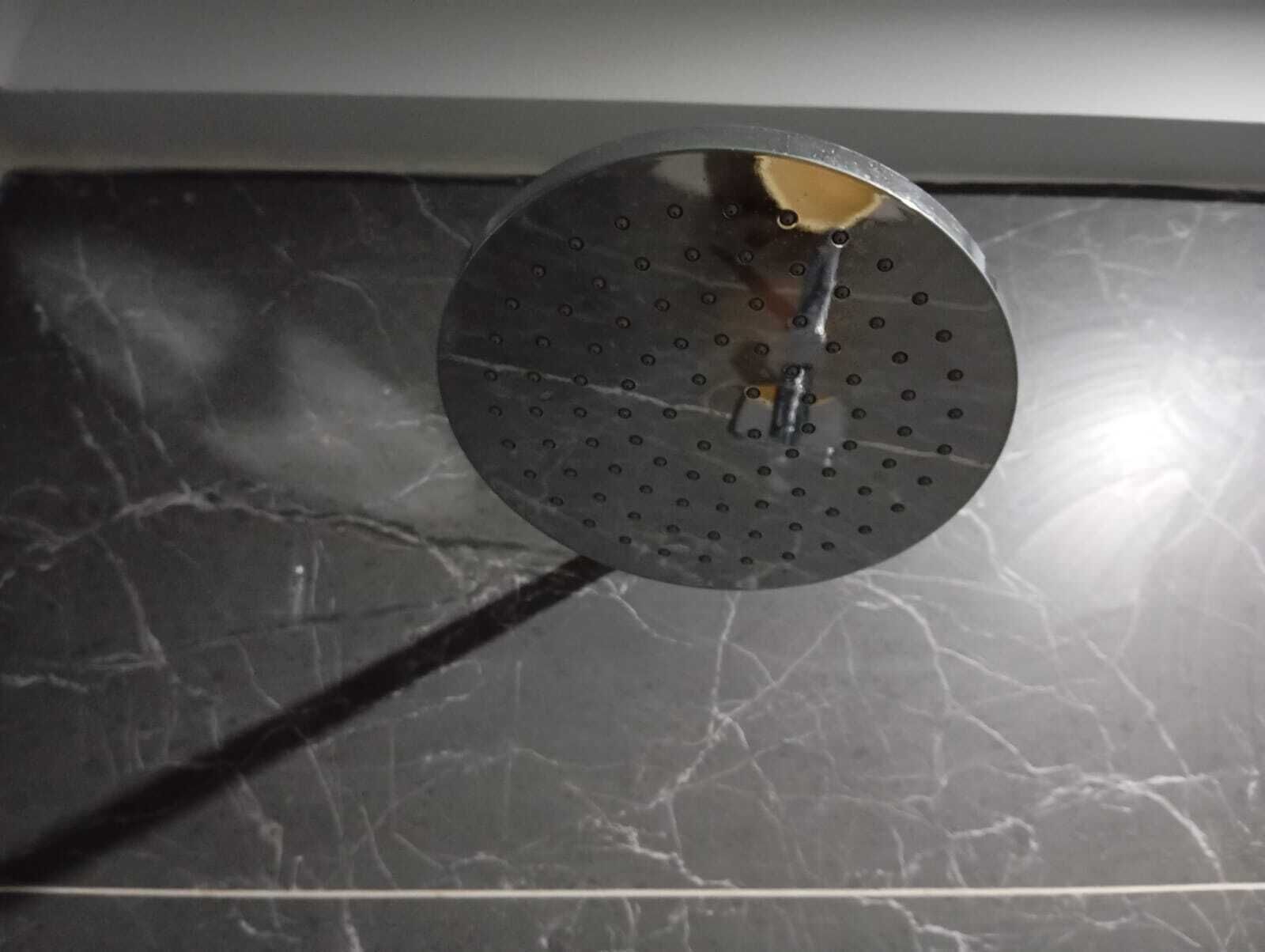 Objeto circular con un agujero central, posiblemente un cabezal de ducha, montado en una pared con un patrón de baldosas de mármol oscuro.