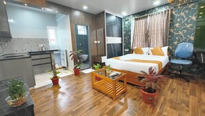 A modern hotel room with a wooden floor, a bed with white bedding and yellow pillows, a desk with a chair, and several potted plants. - Vin Hotels & Service Apartments Manyata Tech Park (Bengaluru)