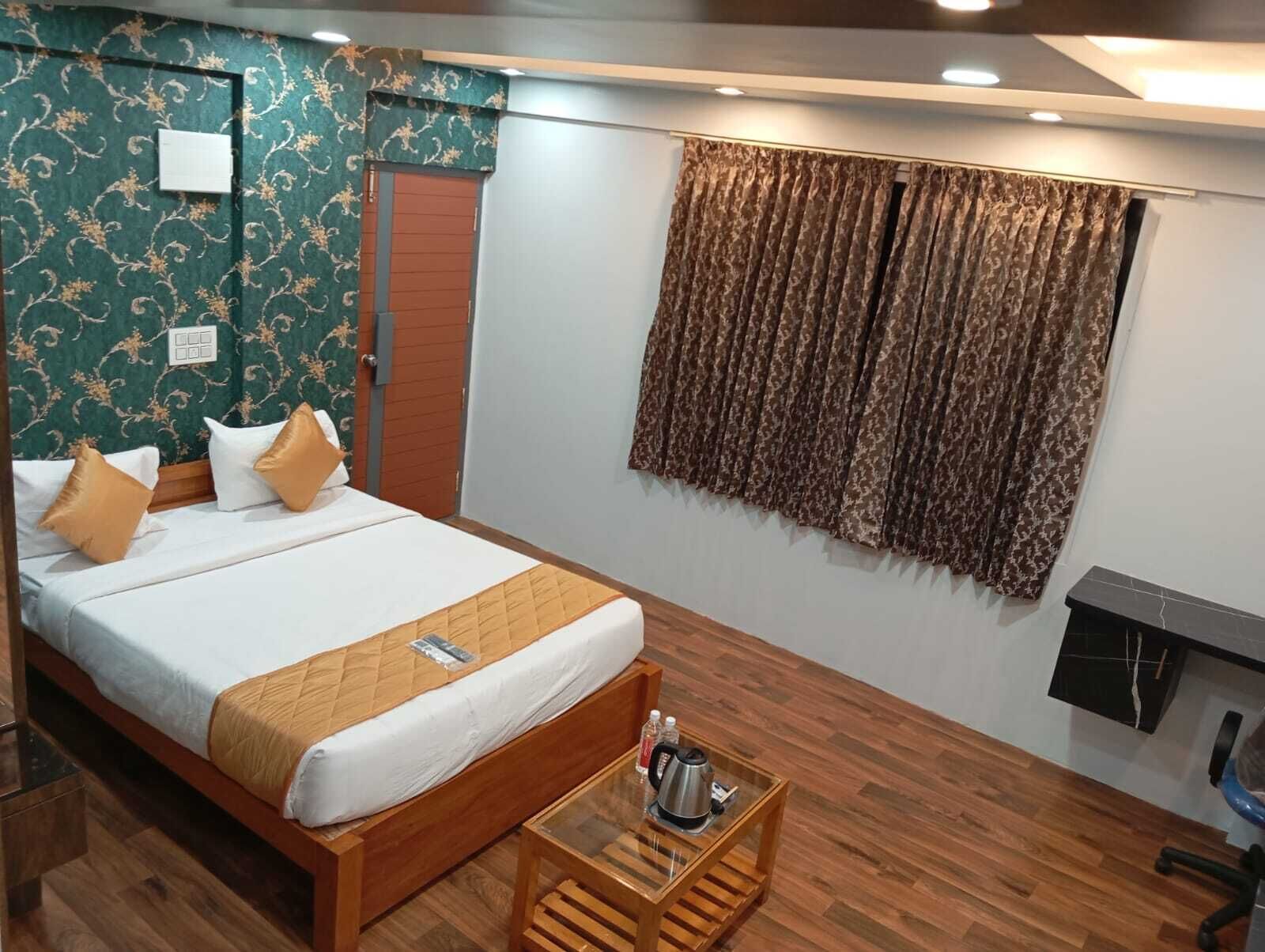 A hotel room with a wooden bed, a glass coffee table, a wooden floor, a patterned wall, and a curtain.