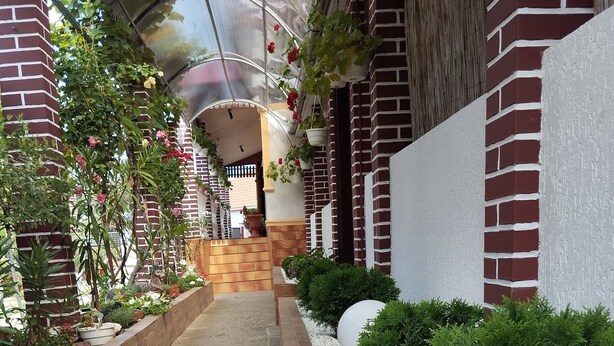 A pathway flanked by brick walls and white pebbles, leading to a covered area with hanging plants and a wooden gate.