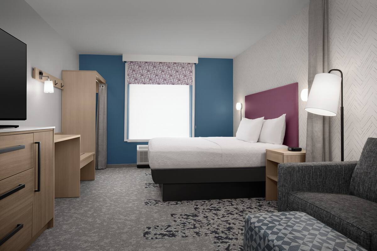 Ein modernes Hotelzimmer mit Bett, Schreibtisch, Stuhl und Fernseher.