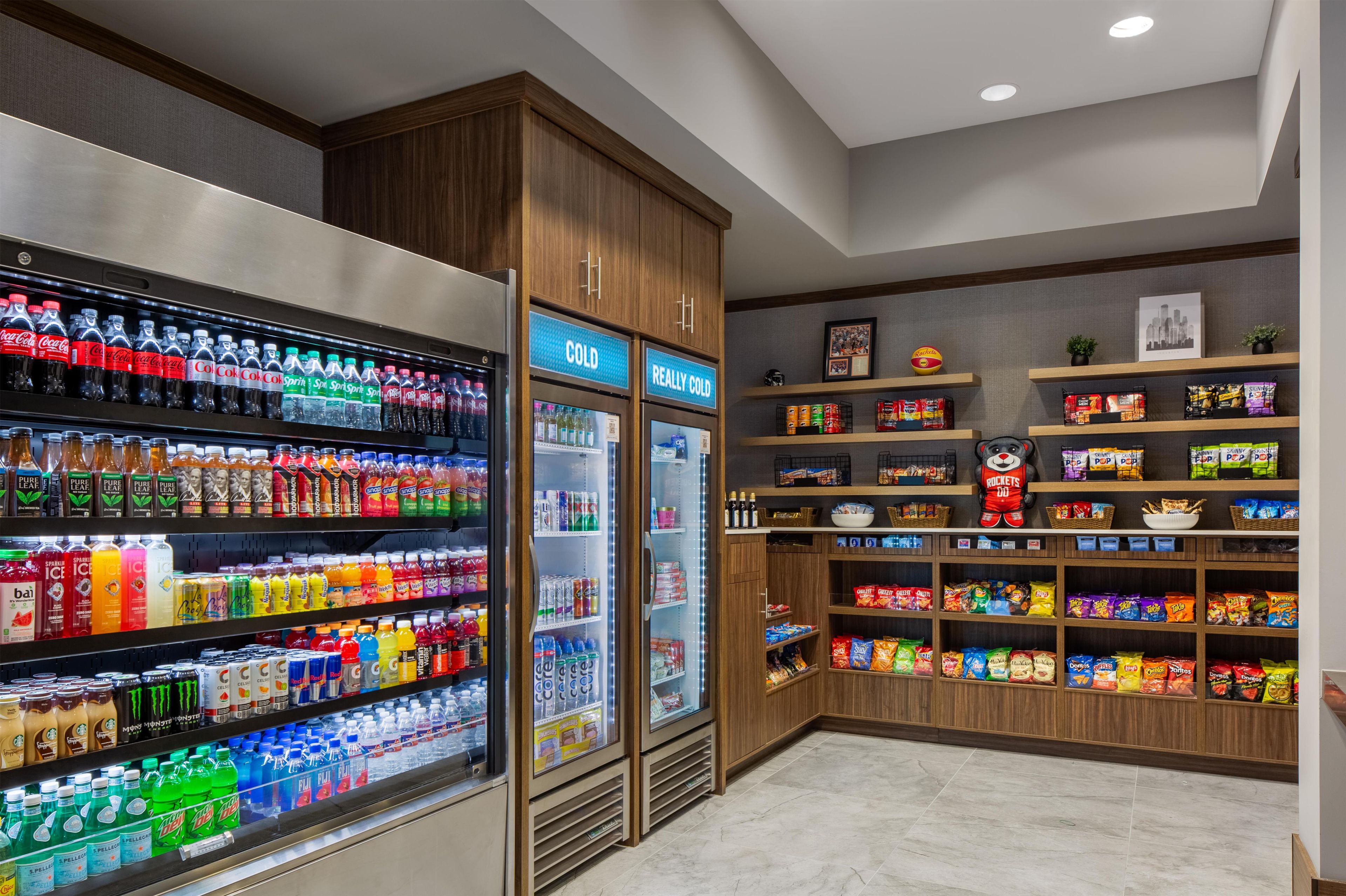 Una sección de bebidas y aperitivos con bebidas refrigeradas y estantes llenos de tentempiés.