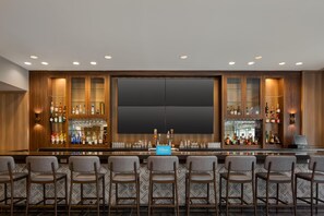 A bar area with a minibar, bar stools, and a large flat-screen TV. - Tru by Hilton Houston Downtown Convention Center (Houston)
