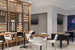 A modern indoor space with a foosball table, white chairs, and a wooden partition with a TV mounted on the wall. - Tru by Hilton Houston Downtown Convention Center (Houston)
