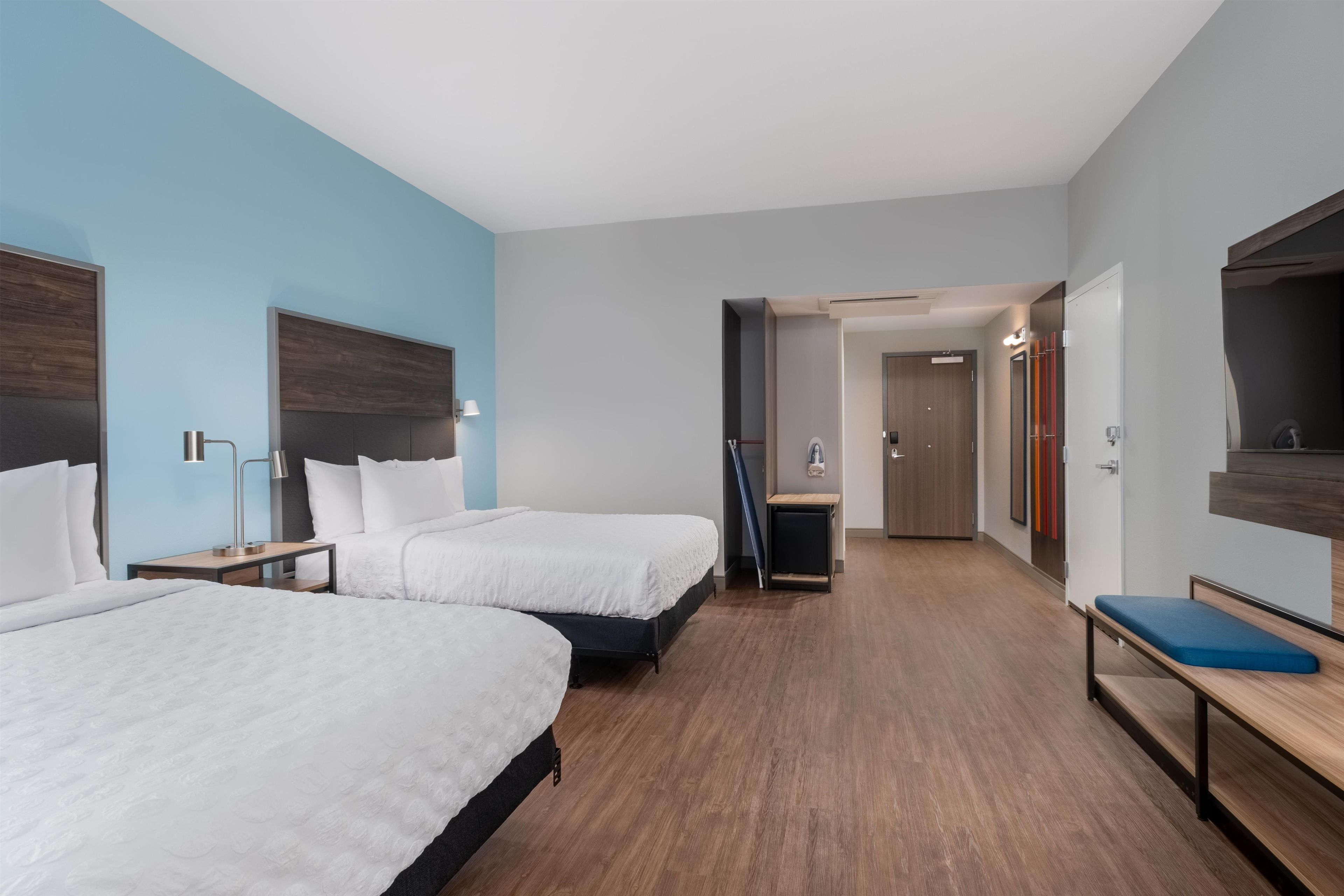 Ein Hotelzimmer mit zwei Betten, einem Schreibtisch, einem Stuhl, einem Spiegel und einer Tür zu einem Badezimmer.