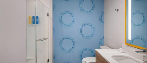 A bathroom with a glass shower enclosure, a toilet, a sink with a mirror, and a wall with a circular pattern.