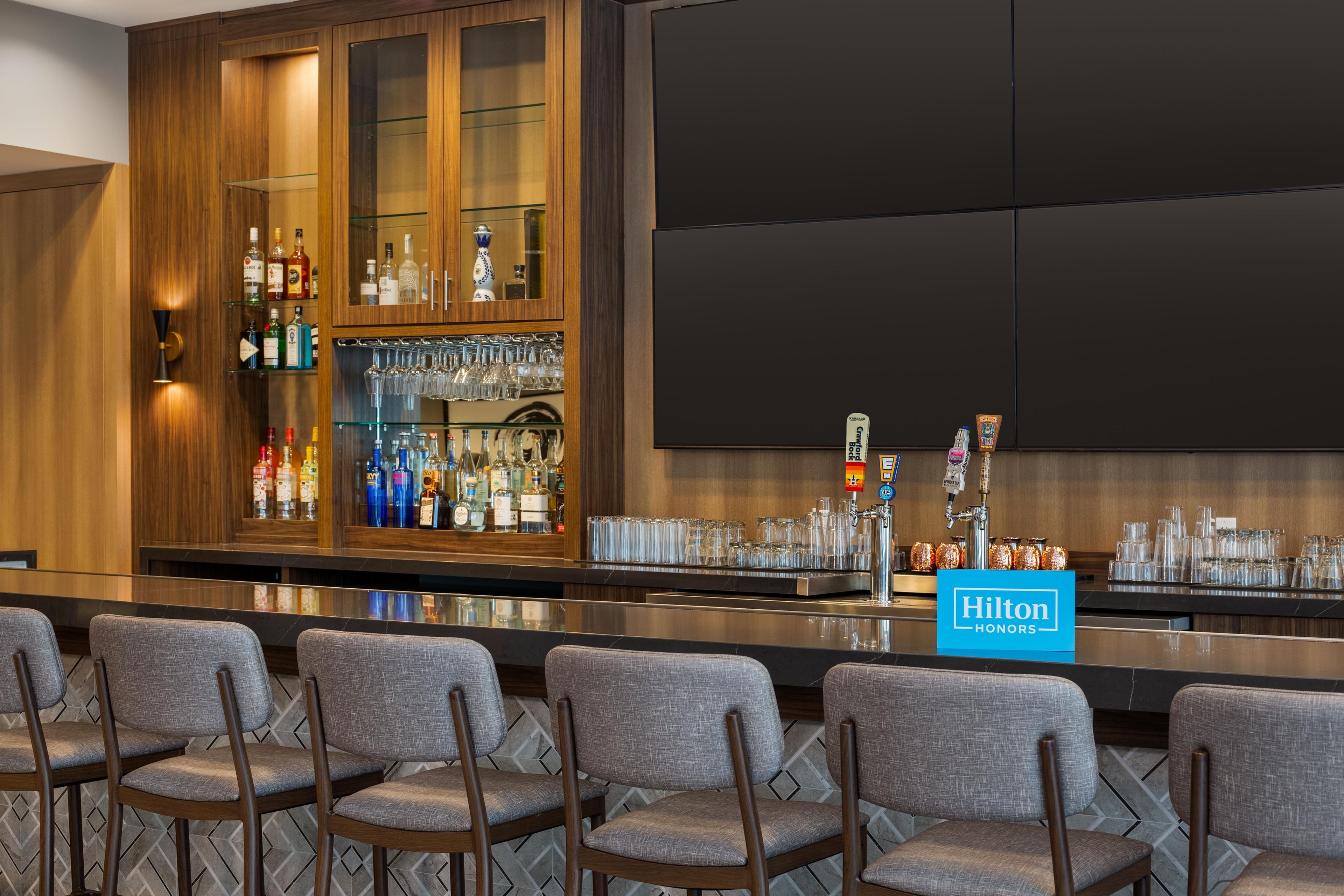 A bar area with a minibar, bar stools, and a minibar cabinet with bottles and glasses.