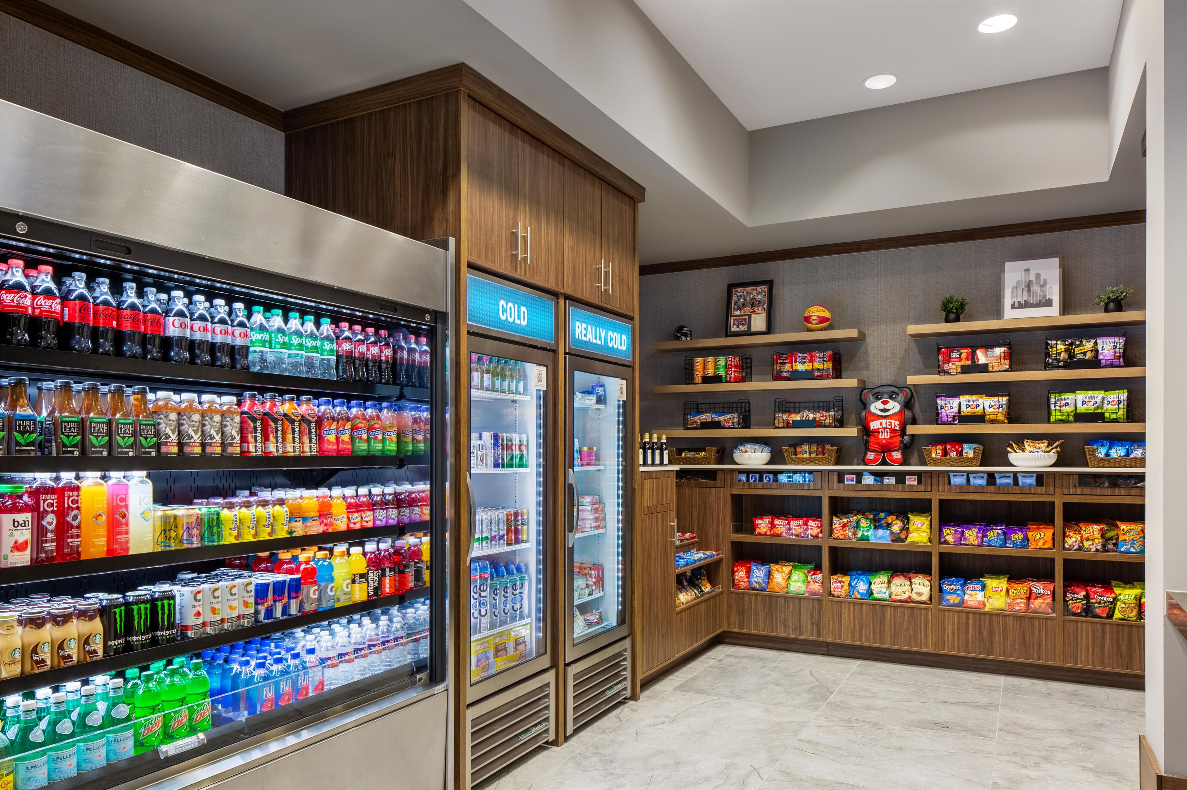Zona de bebidas y aperitivos con bebidas refrigeradas, estantes llenos de bocadillos y una decoración temática deportiva.