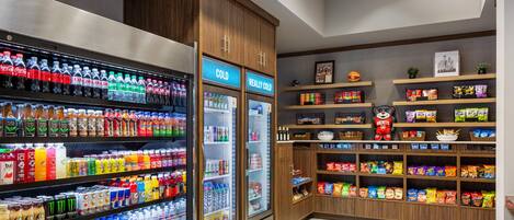 Zona de bebidas y aperitivos con bebidas refrigeradas, estantes llenos de bocadillos y una decoración temática deportiva.