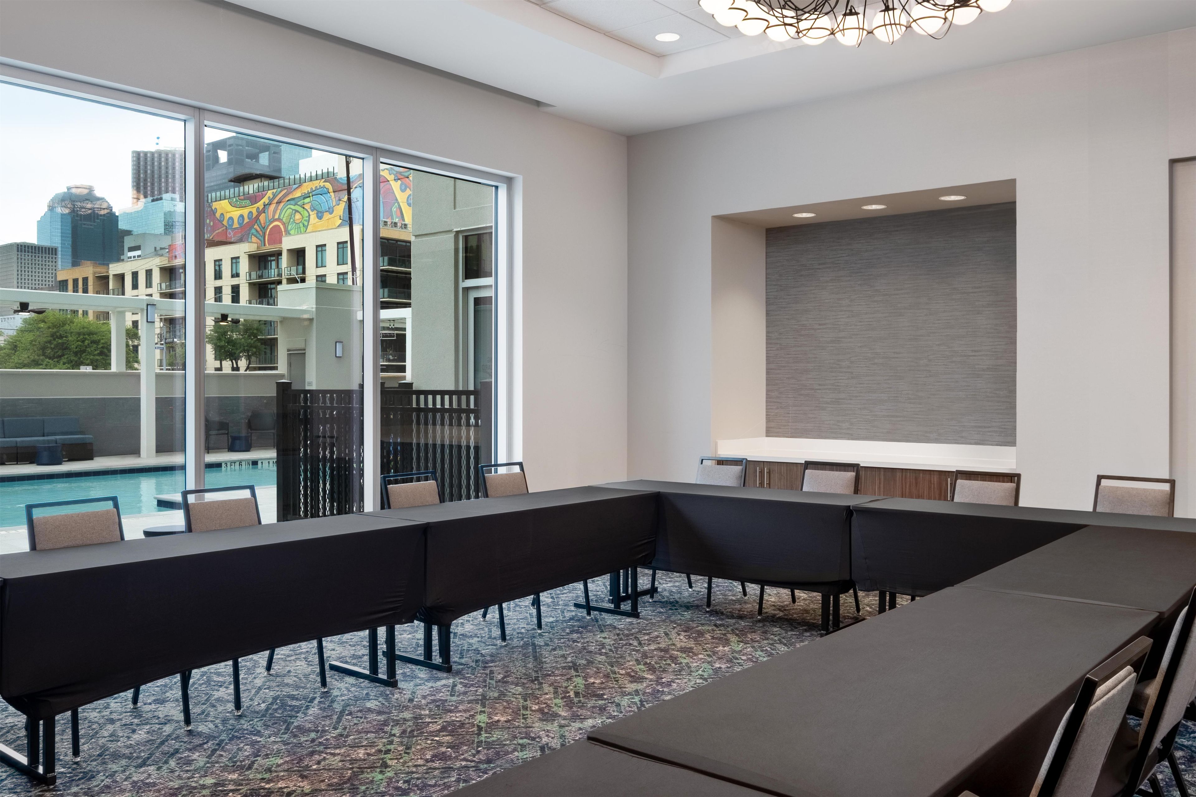 A conference room with a long table and chairs, large windows with a city view, and a modern ceiling light fixture.