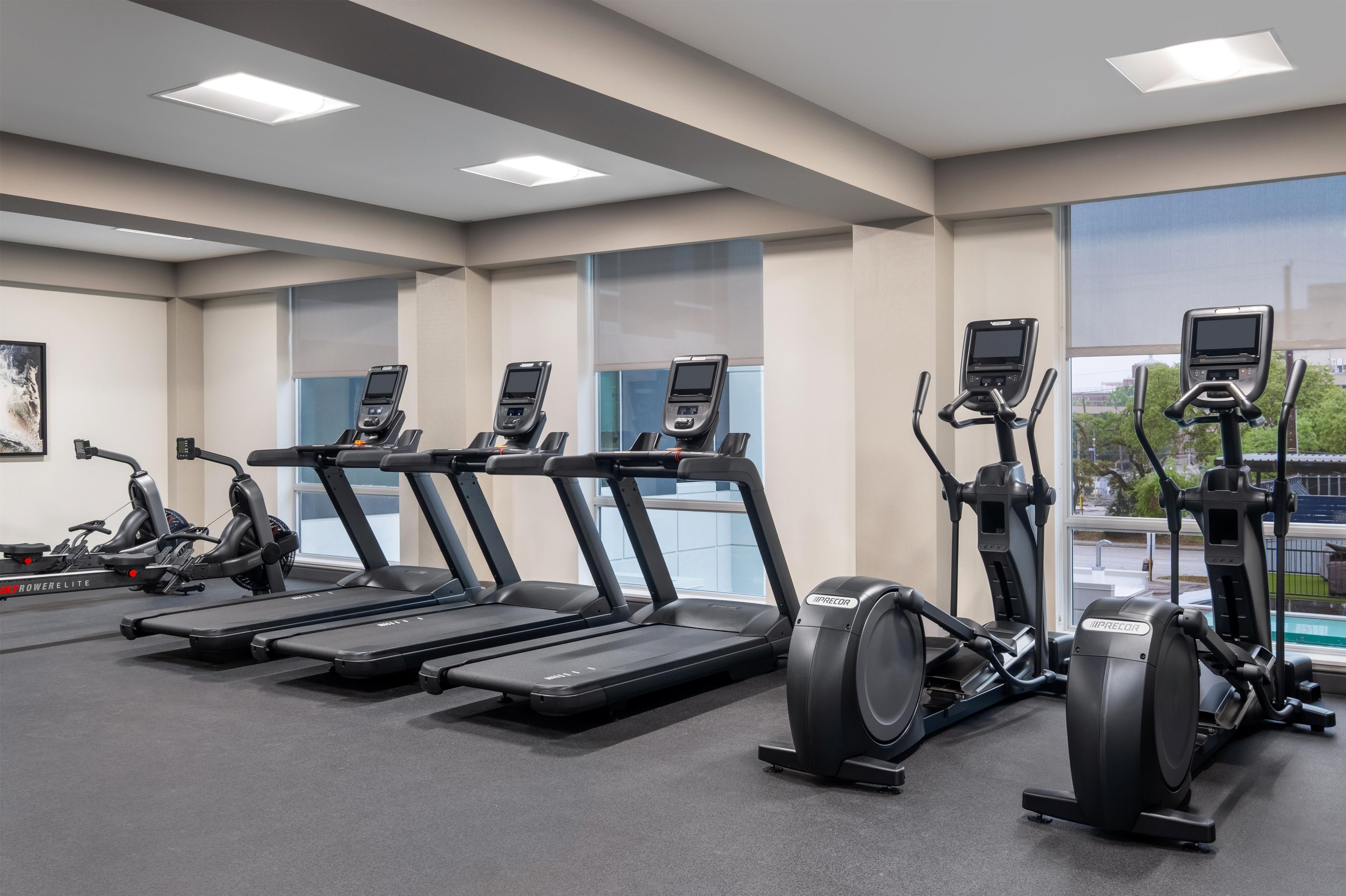 Un gimnasio con cintas de correr, elípticas y bicicletas estáticas, con amplias ventanas y un diseño moderno.