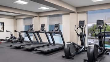 Un gimnasio con cintas de correr, elípticas y bicicletas estáticas, con amplias ventanas y un diseño moderno.