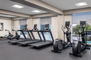 Et fitnesscenter med løbebånd, crosstrainere og spinningcykler, med store vinduer og et moderne design.