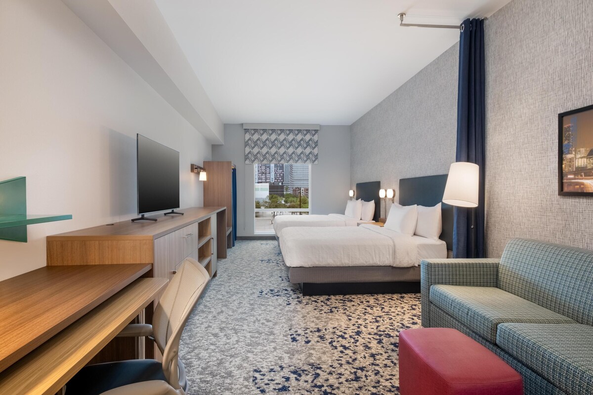 A hotel room with a bed, a desk, a TV, a sofa, and a view of the outdoors.