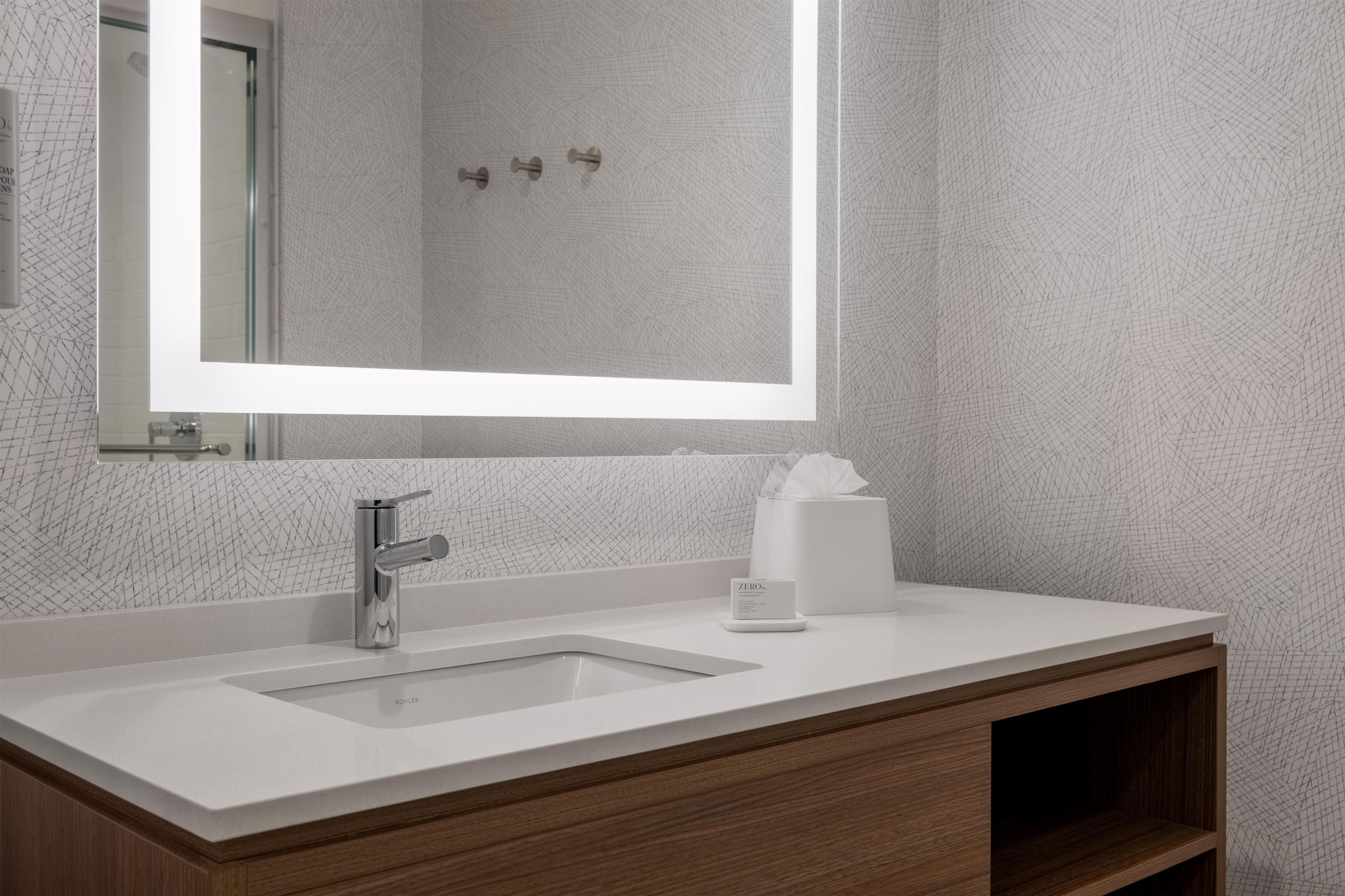 A modern bathroom with a large mirror, a chrome faucet, and a tissue box on the vanity.