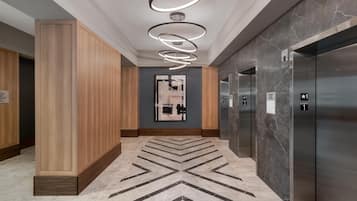 A modern elevator lobby with marble flooring, wooden paneling, and a contemporary light fixture.