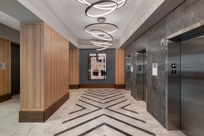 En moderne elevator lobby med marmorgulv, træpaneler og en tidssvarende lampe.