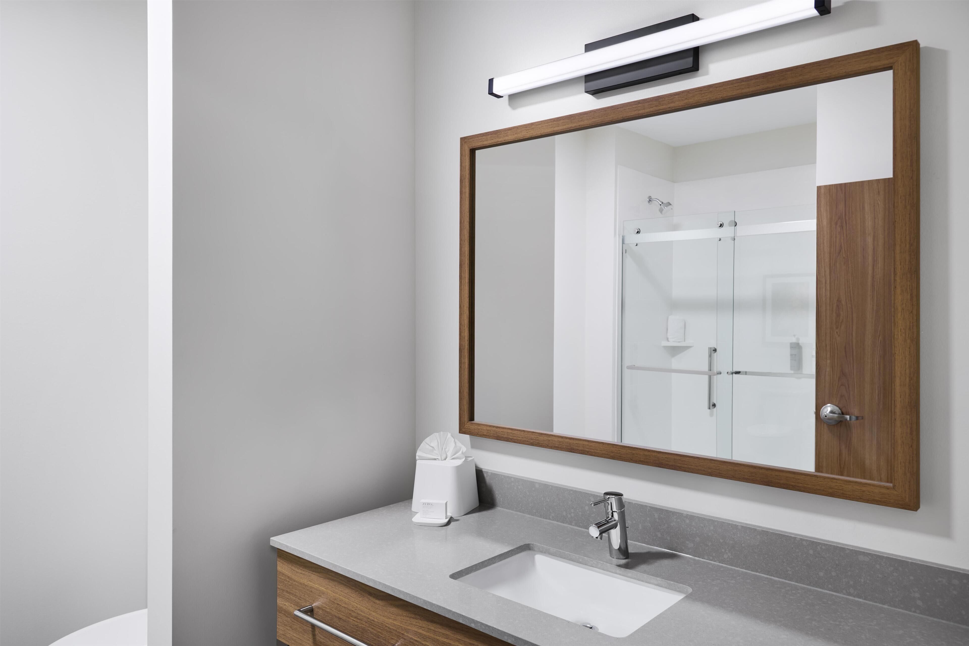 A bathroom with a large mirror, a sink, and a towel dispenser.