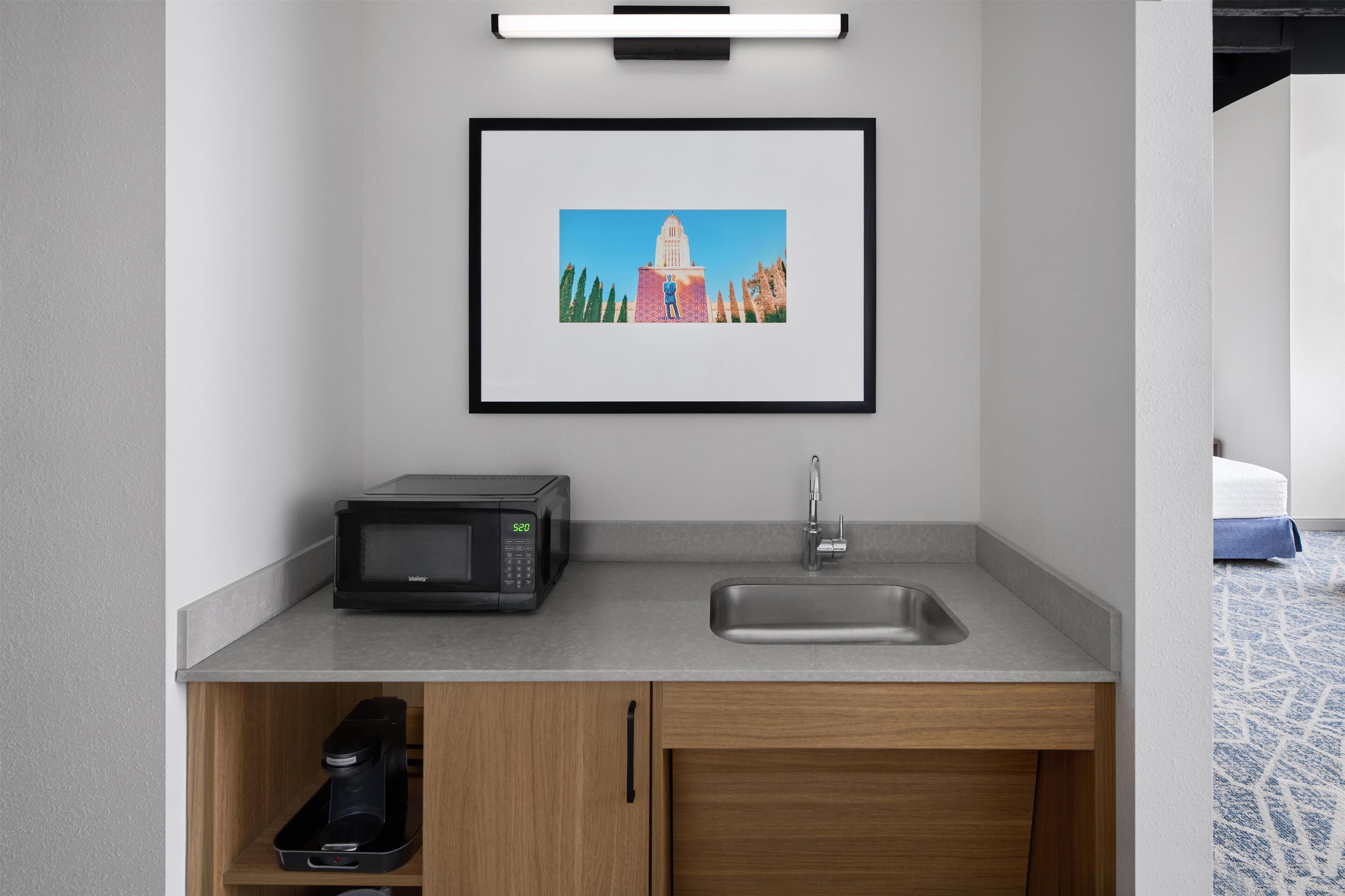 A modern kitchenette with a microwave, sink, and coffee maker.