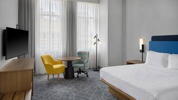 Une chambre d’hôtel équipée d’un lit, d’une télévision, d’un bureau, d’une chaise, d’une table et d’une lampe sur pied.