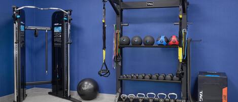 A gym with a squat rack, TRX suspension trainer, and weight plates.
