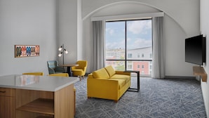 A modern hotel room with a large window, a sofa, a desk, and a flat-screen TV. - Hampton Inn by Hilton Lincoln Downtown (Lincoln)
