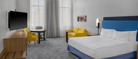 A hotel room with a bed, a desk, a chair, a TV, and a window with curtains.
