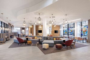A modern hotel lobby with a large seating area, multiple tables, and a high ceiling with unique lighting fixtures. - Hampton By Hilton Tallinn (Tallinn)