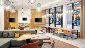 A modern lounge area with a large sofa, multiple tables, and chairs. There are ceiling lights and a large window with a stained glass design. - Hampton By Hilton Tallinn (Tallinn)