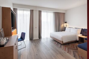 A hotel room with a bed, a desk with a chair, a TV, and a large window with curtains. - Hampton By Hilton Tallinn (Tallinn)