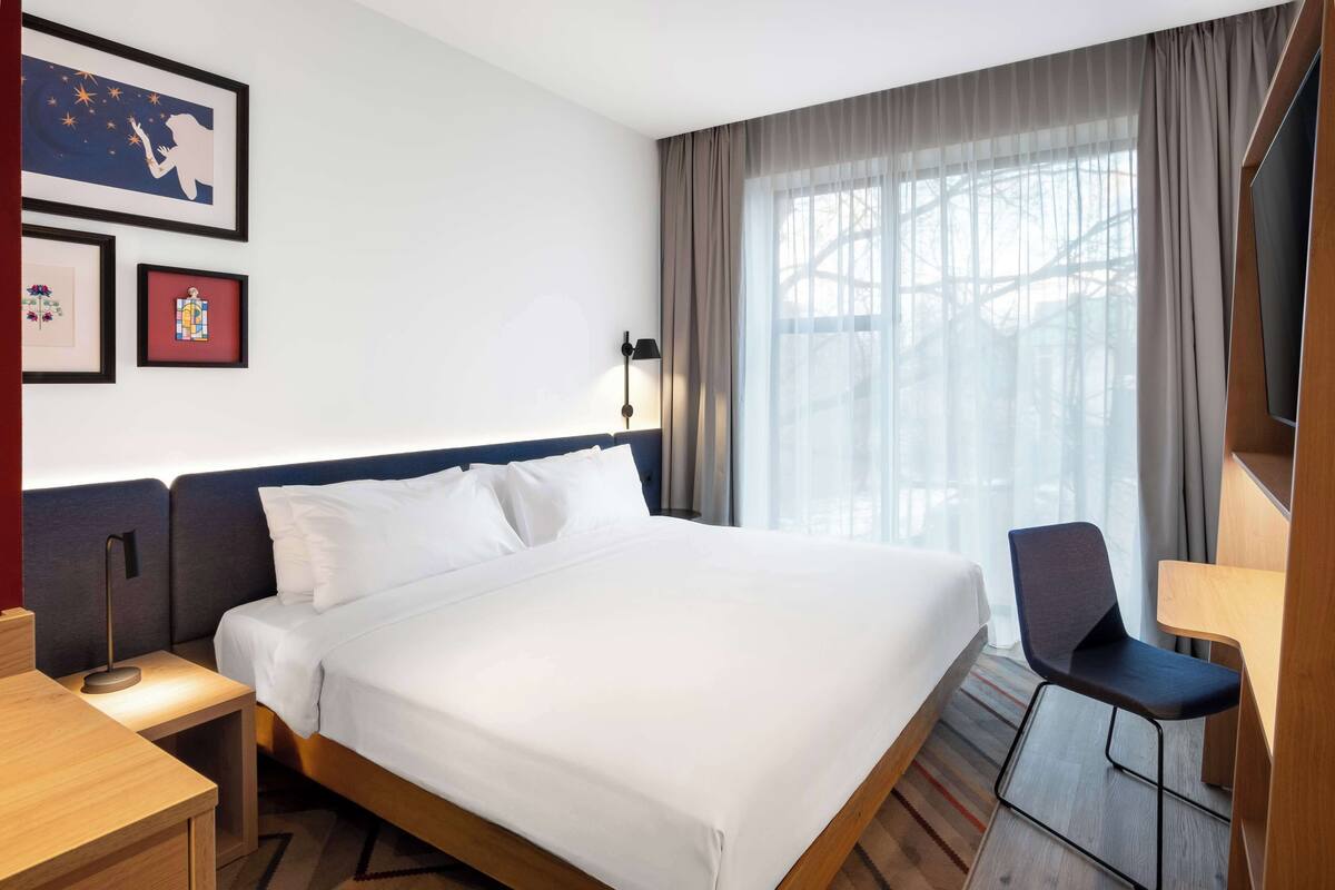 A hotel room with a large bed, a desk, a chair, and a TV.