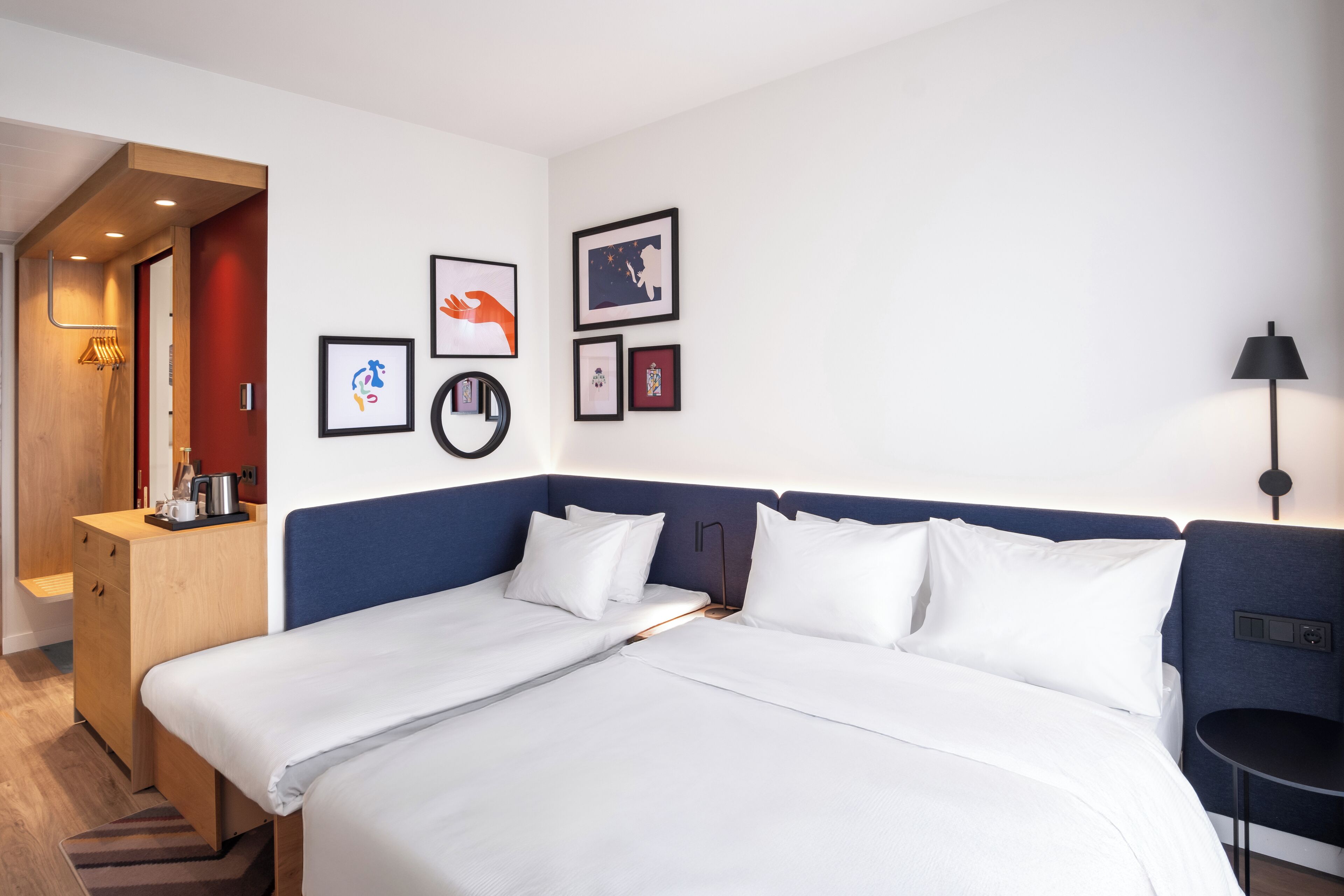 A hotel room with a double bed, a wooden nightstand, a desk, and a small table.